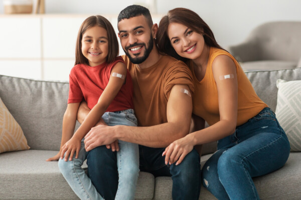 Happy Family with bandaids showing where they got flu shot while they sit on a couch